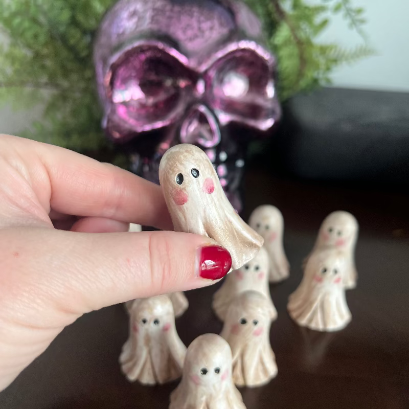 Hand holding a small ghost figurine with a pink skull in the background