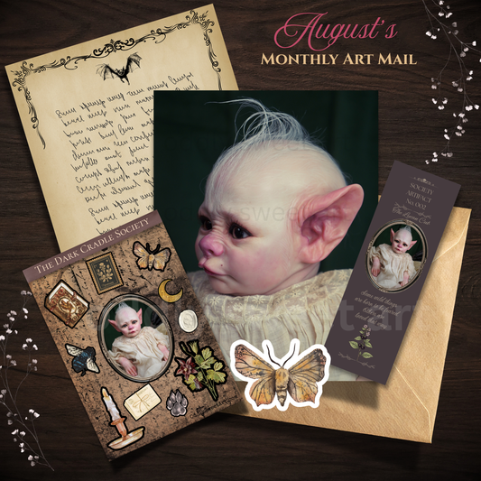 A styled flat lay of gothic art stationery and a central printed card featuring a pale-skinned baby-like creature with large pointed ears. Surrounding elements include a handwritten letter on aged paper, a brown envelope, a decorative card from The Dark Cavalry Society, and a butterfly sticker, all arranged on a dark wood background with the text 'August's Monthly Art Mail' at the top.