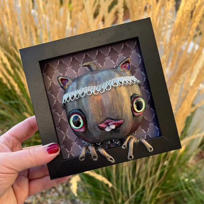 Framed artwork of a creature held by a hand with a natural background