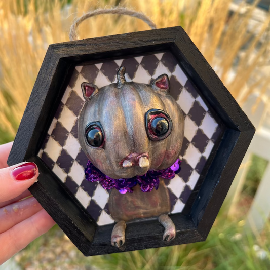 Hexagonal frame with a small animal figurine on a checkered background, held by a hand.