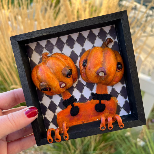 Decorative pumpkin art piece with a black frame held by a hand.