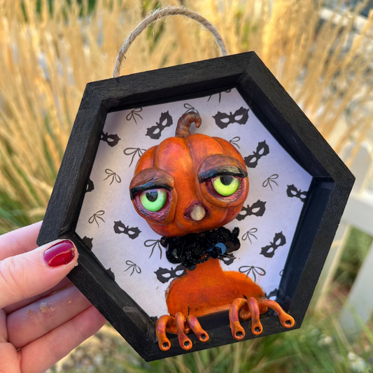 Hexagonal black frame with a pumpkin creature figure against a white background with black cat masks.