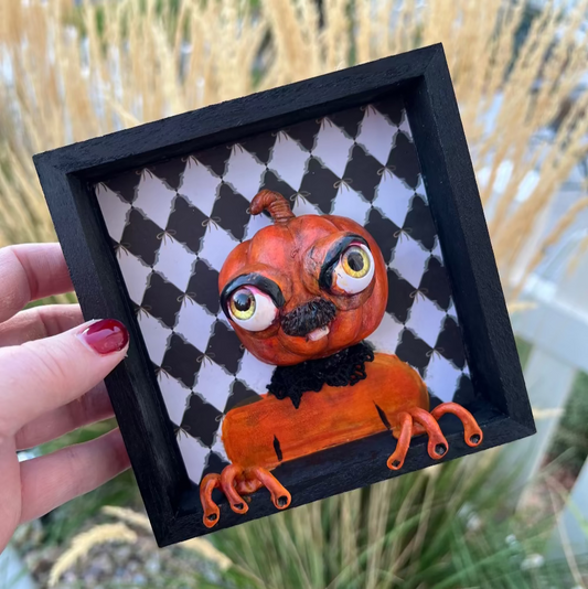 Artistic depiction of a pumpkin with large eyes and orange tentacles on a checkered background, held by a hand.