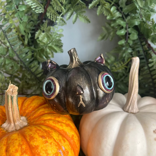 Decorative cat figurine with large eyes surrounded by pumpkins and greenery
