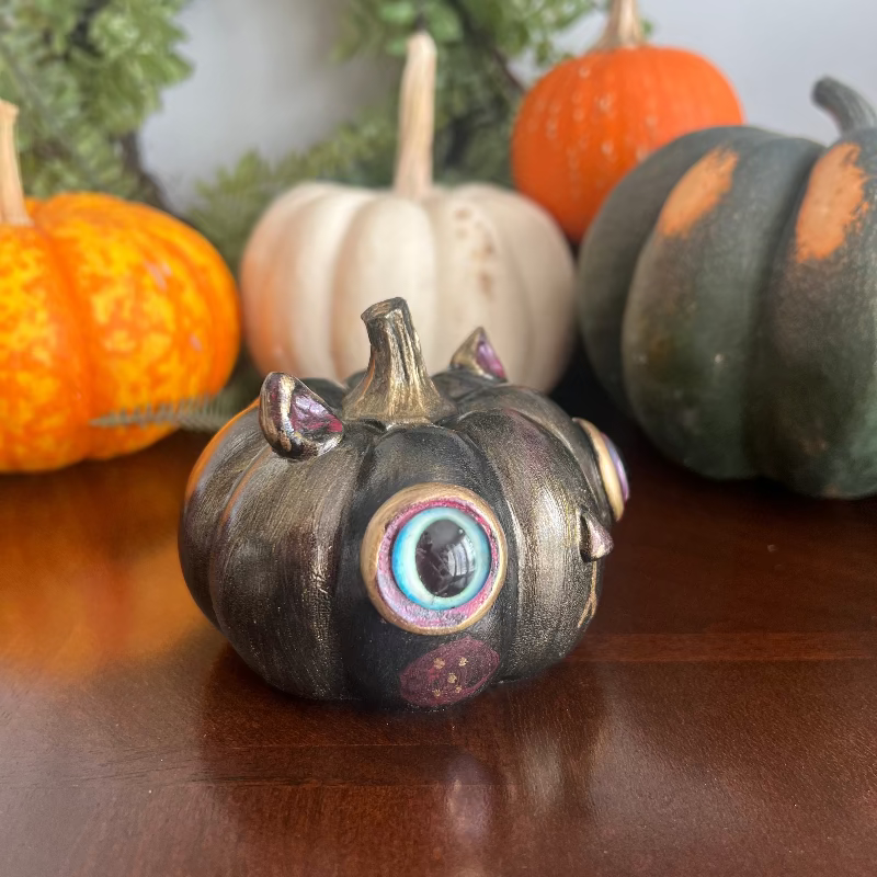 Decorative pumpkin with a multicolored eye surrounded by other pumpkins on a wooden surface.