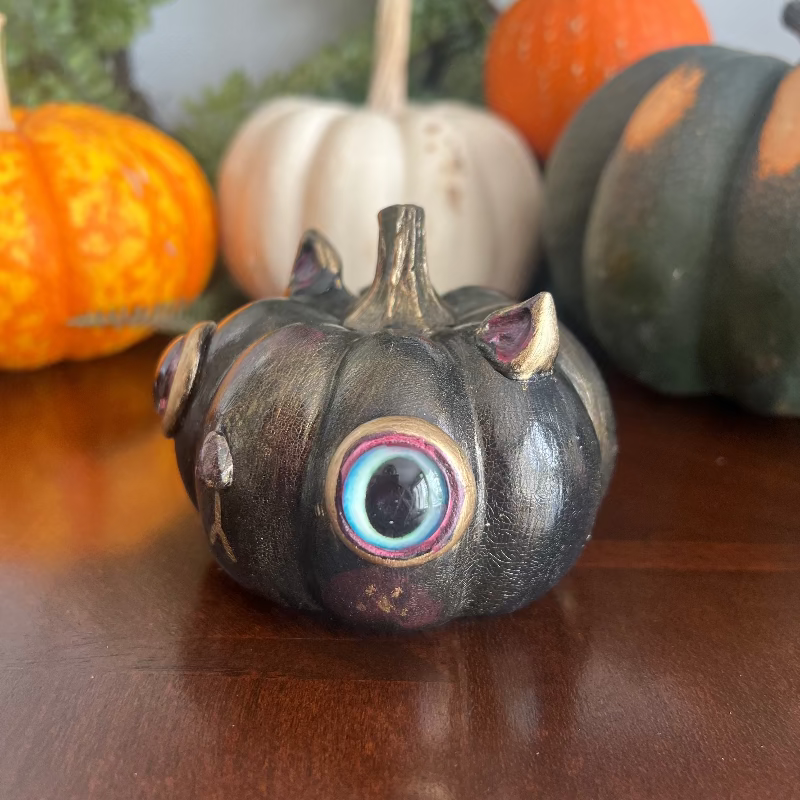 Decorative pumpkin with googly eyes on a wooden surface with other pumpkins in the background.