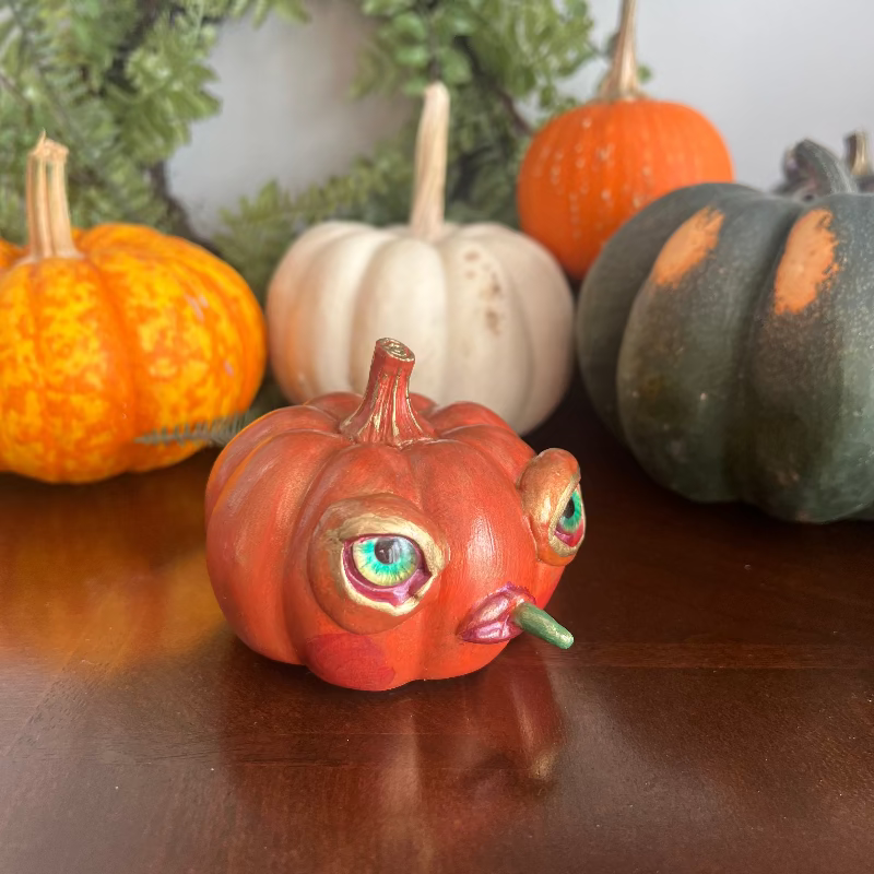 Decorative pumpkin with facial features on a wooden surface with other pumpkins in the background.