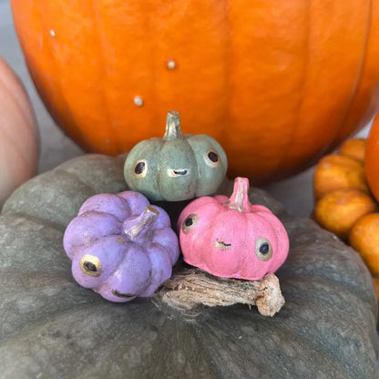 Three small painted pumpkins in purple, green, and pink on a larger pumpkin with a blurred background.