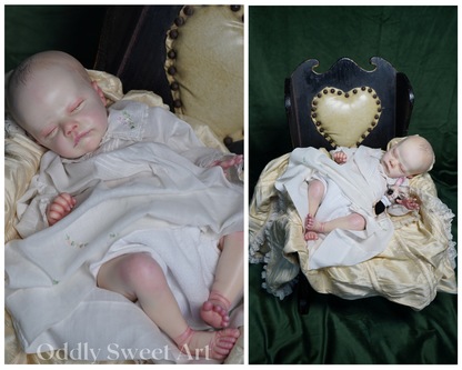 A split-panel product photo showing a realistic sleeping doll or baby figurine dressed in white, posed in two arrangements: on a cream cushion and reclining on a dark wooden chair with a cream heart-shaped backrest, set against a dark green fabric backdrop. The left panel includes the text 'Oddly Sweet Art' at the bottom.