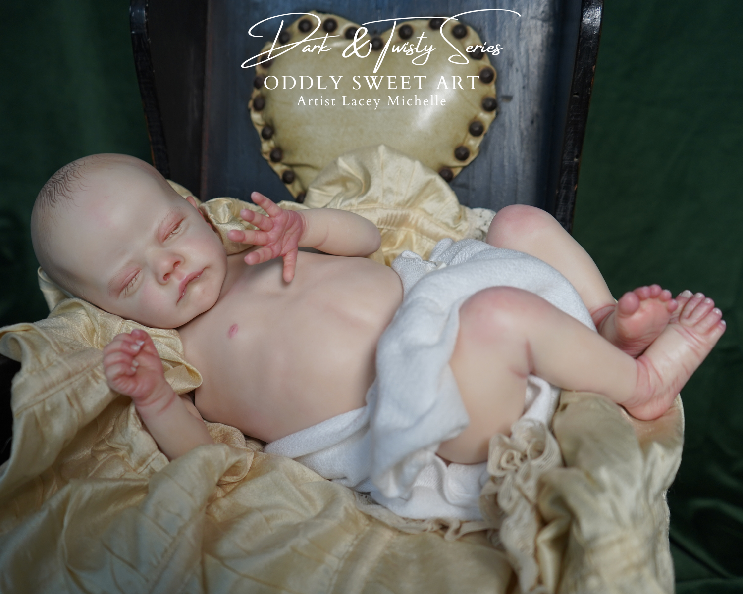 A realistic reborn baby doll lying on its back on a gold satin sheet, positioned in front of a dark wooden chair with a gold tufted backrest. The doll has pale skin, realistic hands, and is wearing a white diaper.