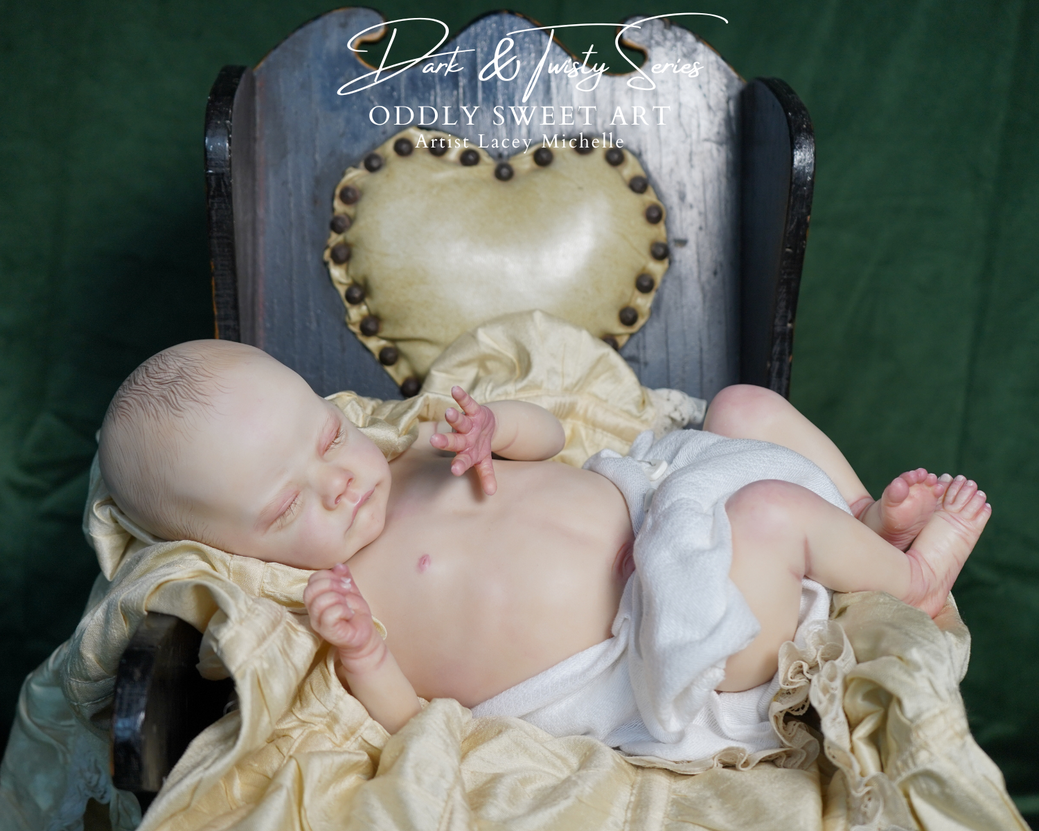 A realistic newborn baby doll or prop baby wrapped in white cloth and draped with cream satin fabric, posed on a dark wooden chair with a heart-shaped cushion against a dark green backdrop. A watermark reads 'Dark & Tidy Sew' and 'ODDITY SWEET ART'.