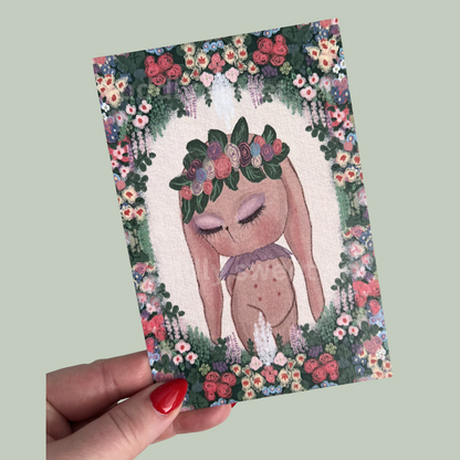 Postcard with a cute illustration of a bunny with a floral crown held by a hand against a light green background.