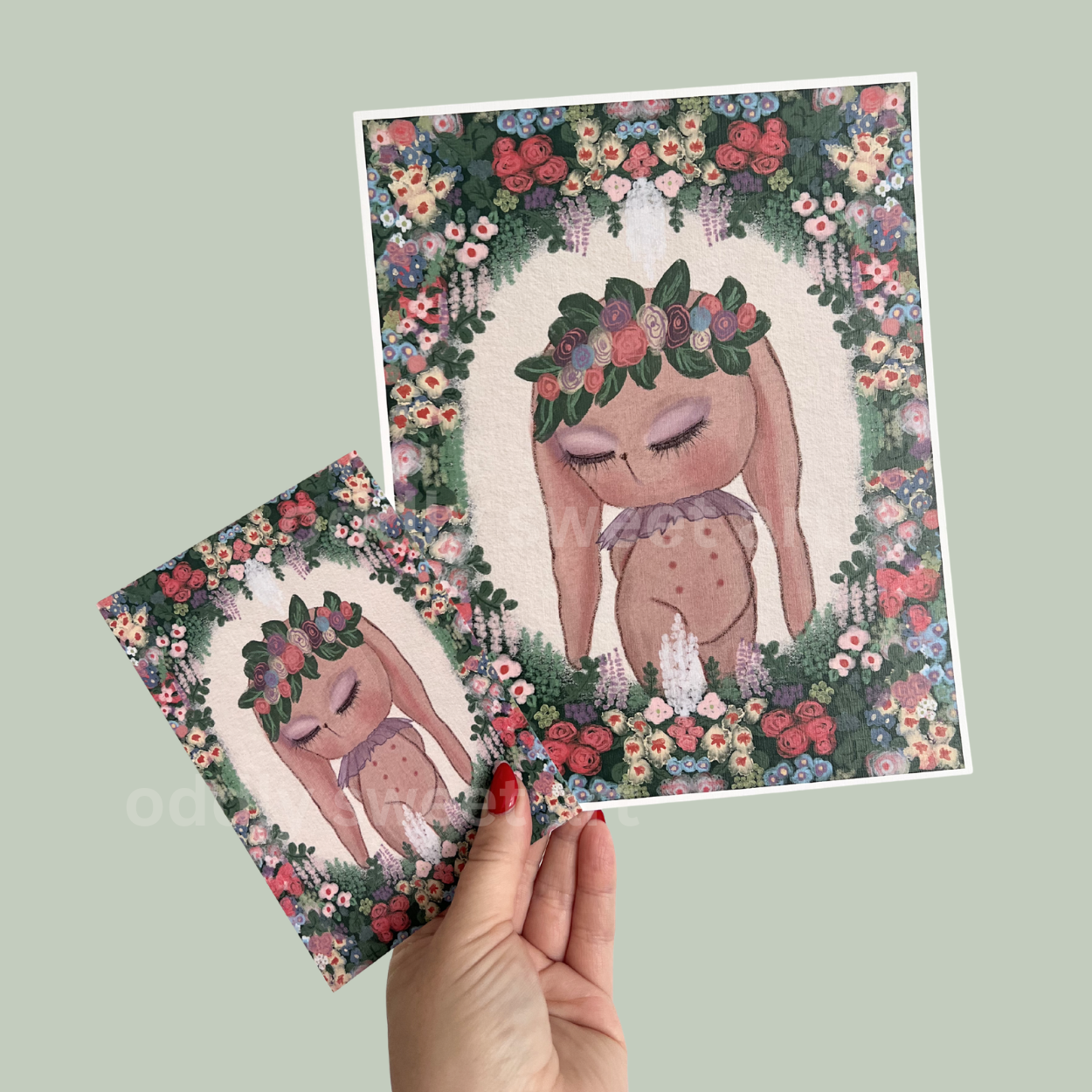 Illustration of a bunny with floral crown on a postcard held by a hand against a light green background