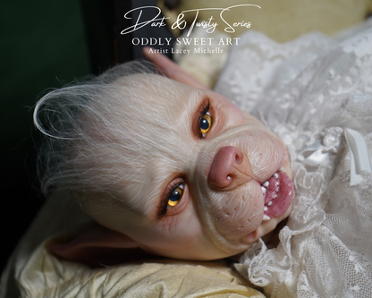 A close-up of a highly realistic animatronic or collectible creature face with pale skin, large amber eyes, pointed ears, and a pink nose, wearing a white lace garment. The image includes the text 'Dart & Twilly Series ODDBY SWEET ART Artist Lacey Michelle' at the top.