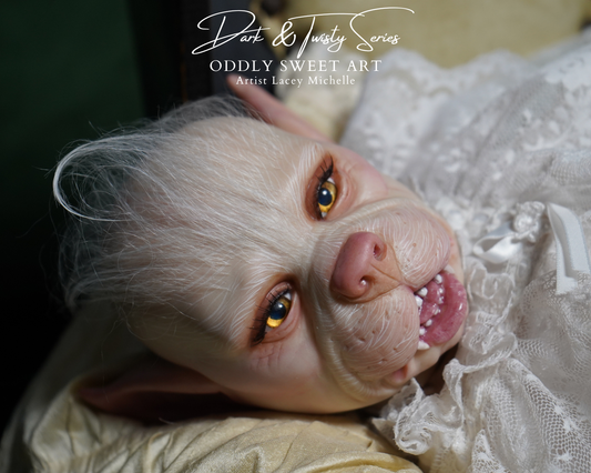 A close-up of a highly realistic animatronic or collectible creature face with pale skin, large amber eyes, pointed ears, and a pink nose, wearing a white lace garment. The image includes the text 'Dart & Twilly Series ODDBY SWEET ART Artist Lacey Michelle' at the top.