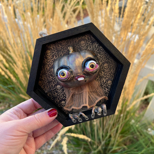 Hexagonal framed artwork of a pumpkin held by a hand with a natural background