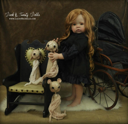 A posed doll scene with a large doll in a black dress holding a pale stitched mouse, next to a small doll on a chair and another stitched mouse on the floor. A vintage pram is visible in the background against a brown backdrop.