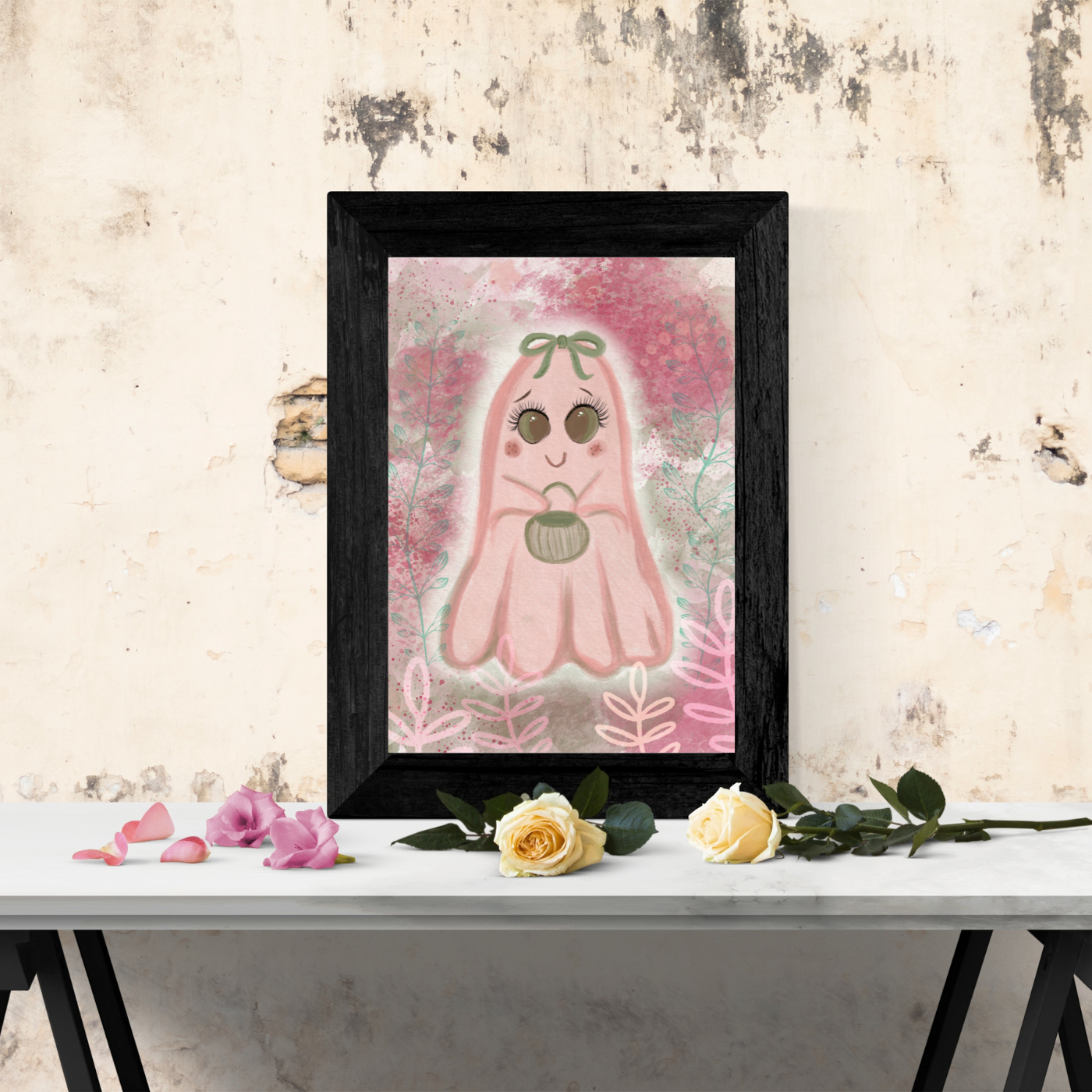 pink ghost holding a green candy bucket  in black frame on table top of yellow roses